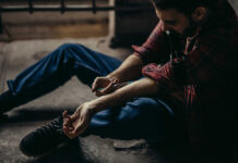 man sitting on floor injecting his arm with a syringe