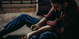 man sitting on floor injecting his arm with a syringe