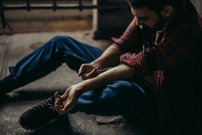 man sitting on floor injecting his arm with a syringe