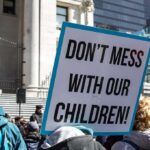 Parental Rights Collision—Education Dept Steps In protest sign held in a crowd outside a government building