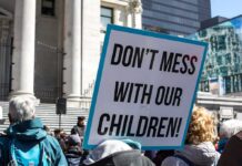 Parental Rights Collision—Education Dept Steps In protest sign held in a crowd outside a government building