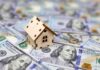 Tax The Rich Becomes Dox The Middle Mini wooden house on scattered US hundred-dollar bills