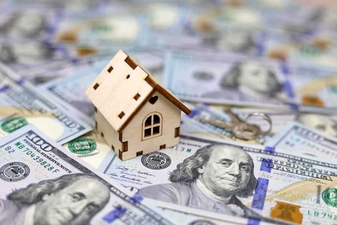 shutterstock_2113109222 Mini wooden house on scattered US hundred-dollar bills
