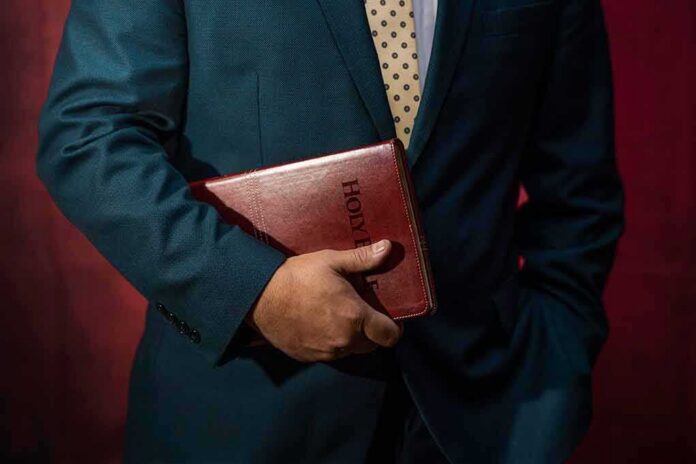 shutterstock_2220699155 Person in a suit holding a red leather Bible