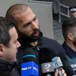 Man speaking to reporters with microphones outside a building