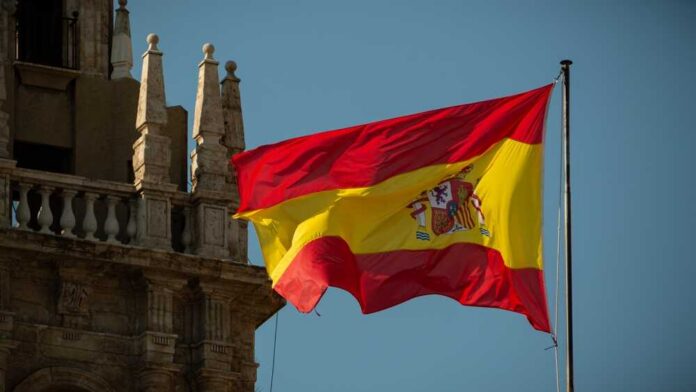Spanish,Flag,Waving,In,Front,Of,A,Cathedral Spanish flag waving against a clear blue sky