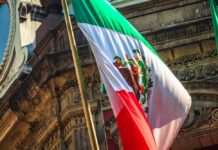 Preventable Deaths Exposed—ICE Under Fire Mexican flag waving in front of an ornate stone building