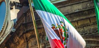 Mexican flag waving in front of an ornate stone building