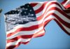 Flag Insult Fallout—Party Doubles Down Waving American flag against a clear blue sky