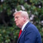 Trump Blasts NATO Spending As ‘Ridiculous’ Profile view of a man in formal attire with a light-colored suit and red tie against a green background