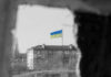 Ukraine Sacrificed? Trump’s Plan Stuns Allies Ukraine flag on building seen through dark frame.