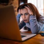 Woman holding head while looking at laptop