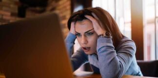 Woman holding head while looking at laptop