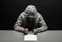 12-Year-Old Charged In Deadly D.C. Shooting Person in gray hoodie writing while handcuffed at a table