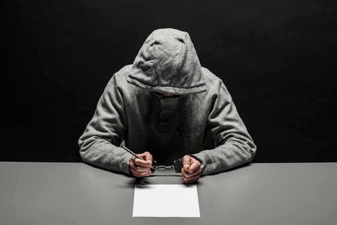shutterstock_1074311507 Person in gray hoodie writing while handcuffed at a table