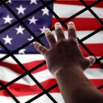 ICE Hunger Strikes Meet Restraints Hand reaching through fence toward American flag
