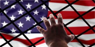 Hand reaching through fence toward American flag