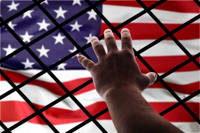 shutterstock_1116440492 Hand reaching through fence toward American flag