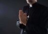 Clergyman in black robe praying with hands together