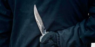 Gloved hand holding a serrated knife against a dark jacket