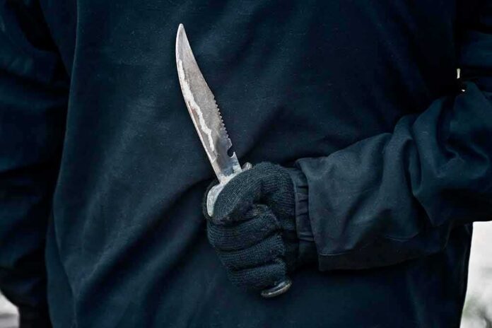 Gloved hand holding a serrated knife against a dark jacket