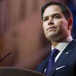 Sanctions Squeeze Tightens — Missiles On Hold man in suit speaking at podium