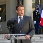 man in suit speaking at podium with microphones