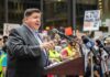 Speaker at a podium addressing a crowd with microphones and protest signs