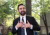 Court Twist Keeps Costly Surcharge Alive Man in suit speaking with hands on chest outdoors