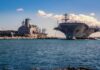 Aircraft carrier and support ships docked at a naval harbor