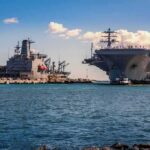 Evacuated – Bahrain Exodus, No Way Home Aircraft carrier and support ships docked at a naval harbor