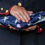Pentagon Reversal: B‑1s Back In Action Uniformed person holding a folded American flag