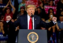 Donald Trump speaking at a rally podium with arms raised