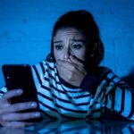woman covering mouth while looking at smartphone