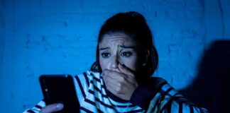 woman covering mouth while looking at smartphone