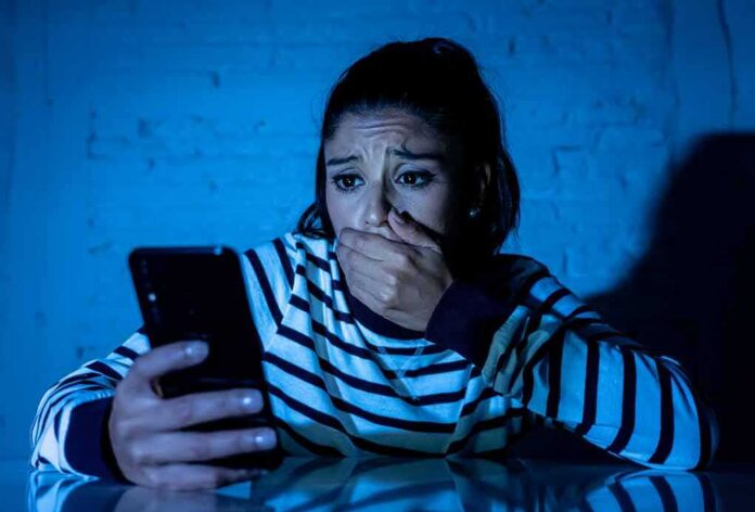woman covering mouth while looking at smartphone