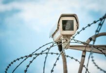 Security camera above barbed wire against blue sky
