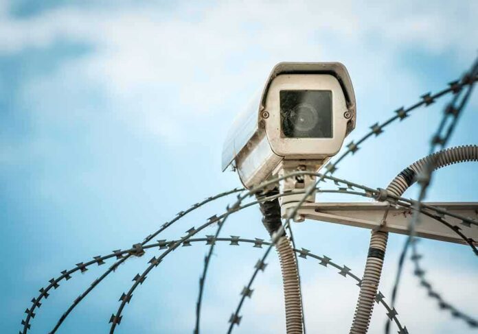Security camera above barbed wire against blue sky