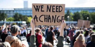 Person holding protest sign above head at a crowded rally