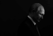 Vladimir Putin in profile, side-lit against a dark background