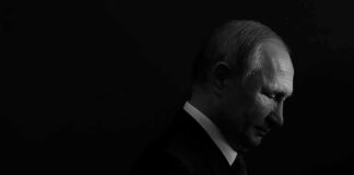 Vladimir Putin in profile, side-lit against a dark background
