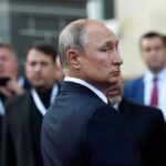 Russia’s Rarest Jet Strikes From Sanctuary man in suit looking back in a crowd