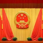 Chinese national emblem on red-draped stage backdrop