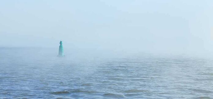 Green buoy in foggy sea