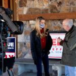 Likely D Label Lights Conservative Fire Kelly Loeffler speaks with a man during an on-camera interview at a stone-walled venue