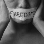 person with taped mouth holding their face