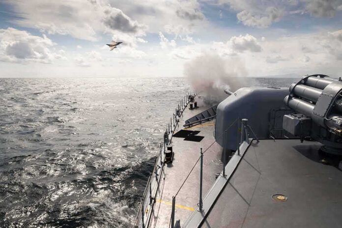 shutterstock_2129183807 naval warship firing deck gun at sea