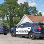 Coach’s Son Arrested After Home Shooting Two police SUVs parked near a suburban house