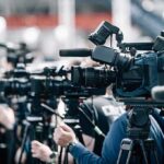 CIA Ties Surface: Feminist Icon in Crosshairs Broadcast cameras on tripods at a press event