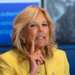 woman in yellow blazer gesturing with raised index finger
